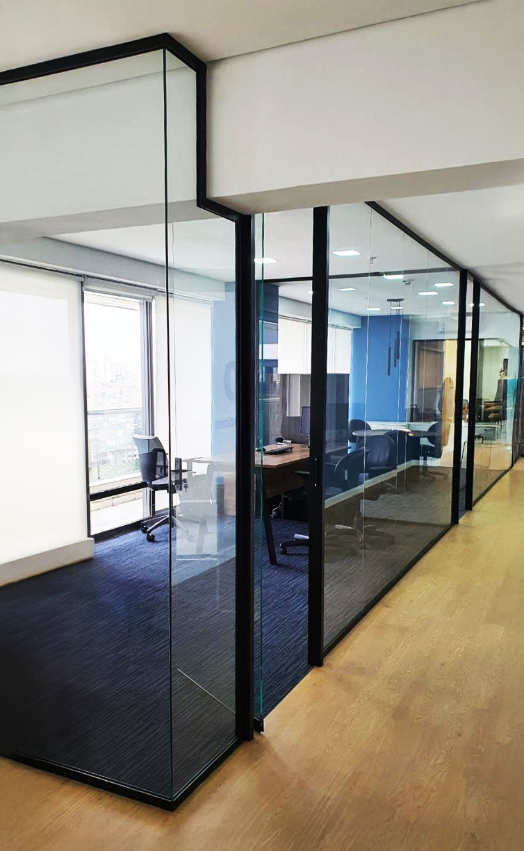Ambiente corporativo com a elegante divisória Solid Dual 53mm na cor preta, porta de vidro e carpete azul na parte interna, contrastando com o piso madeira da parte externa.