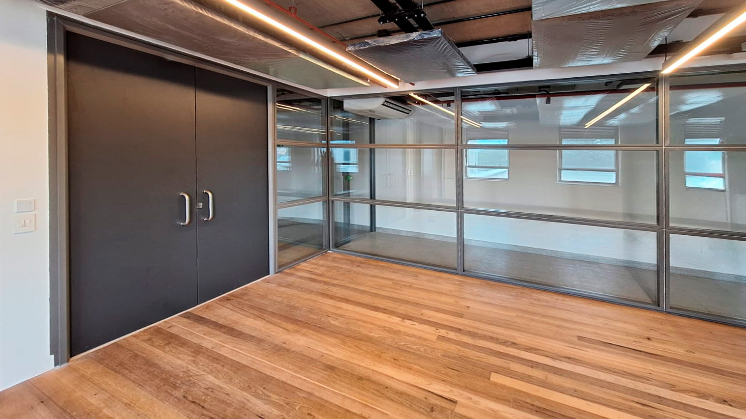 Divisão de ambiente grande com porta dupla na cor preta, com dois puxadores modernos prata. As divisórias no estilo grade, com suportes transversais e horizontais e vidros sem cor, acompanham a porta com encaixe perfeito.