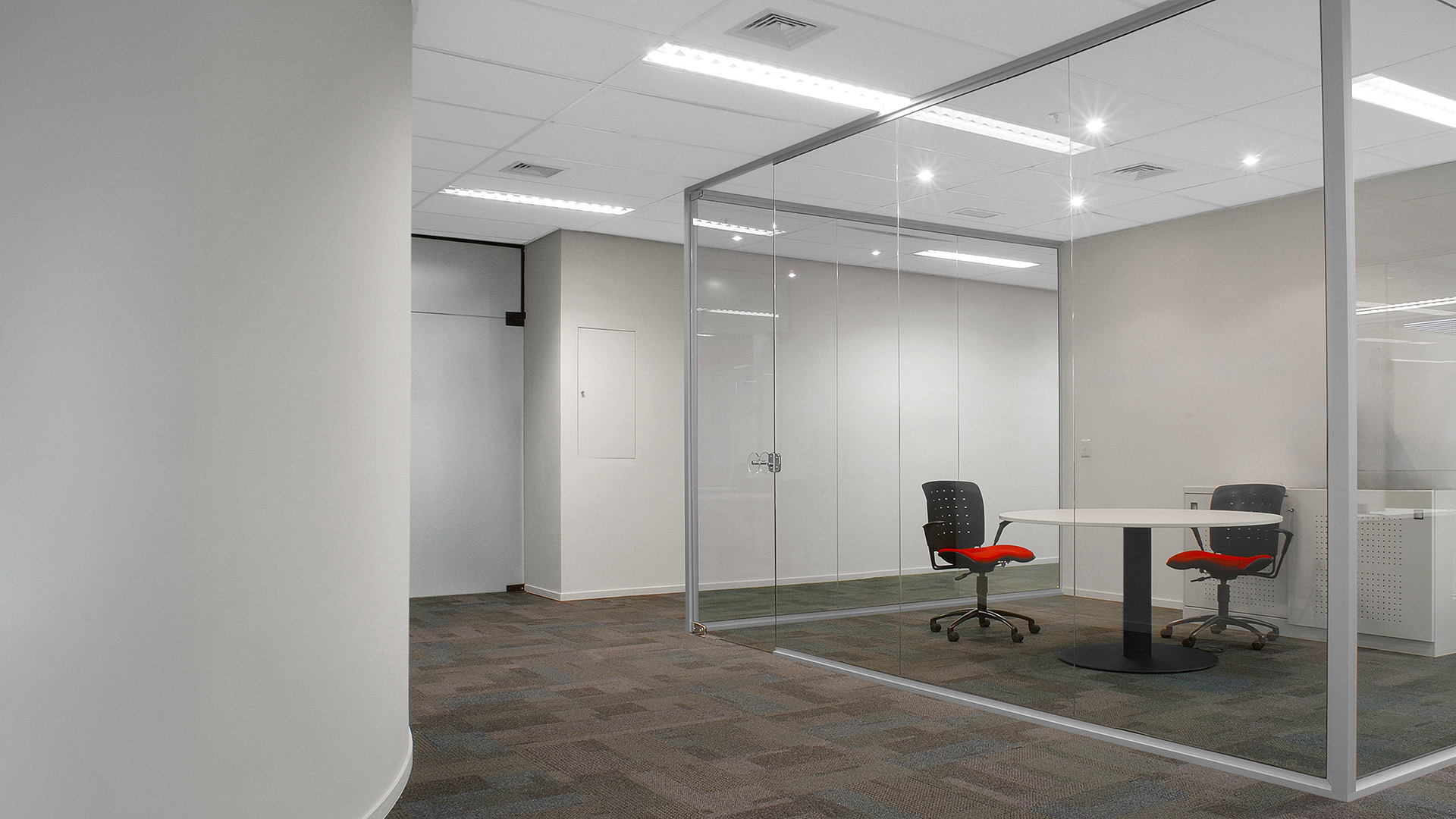 Ambiente de escritório com carpete cinza e sala construída com divisórias Solid, em estrutura branca e vidro tranparente.